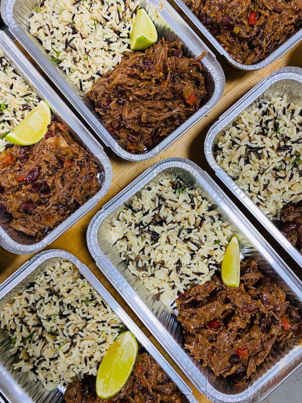 Photograph from above of several metal takeaway trays containing pulled beef chilli and coriander wild rice