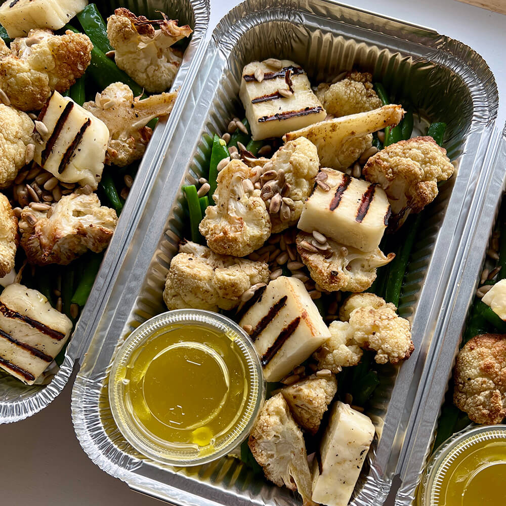 Photograph of a halloumi, green bean, roasted cauliflower and mixed seed salad in a metal takeaway container